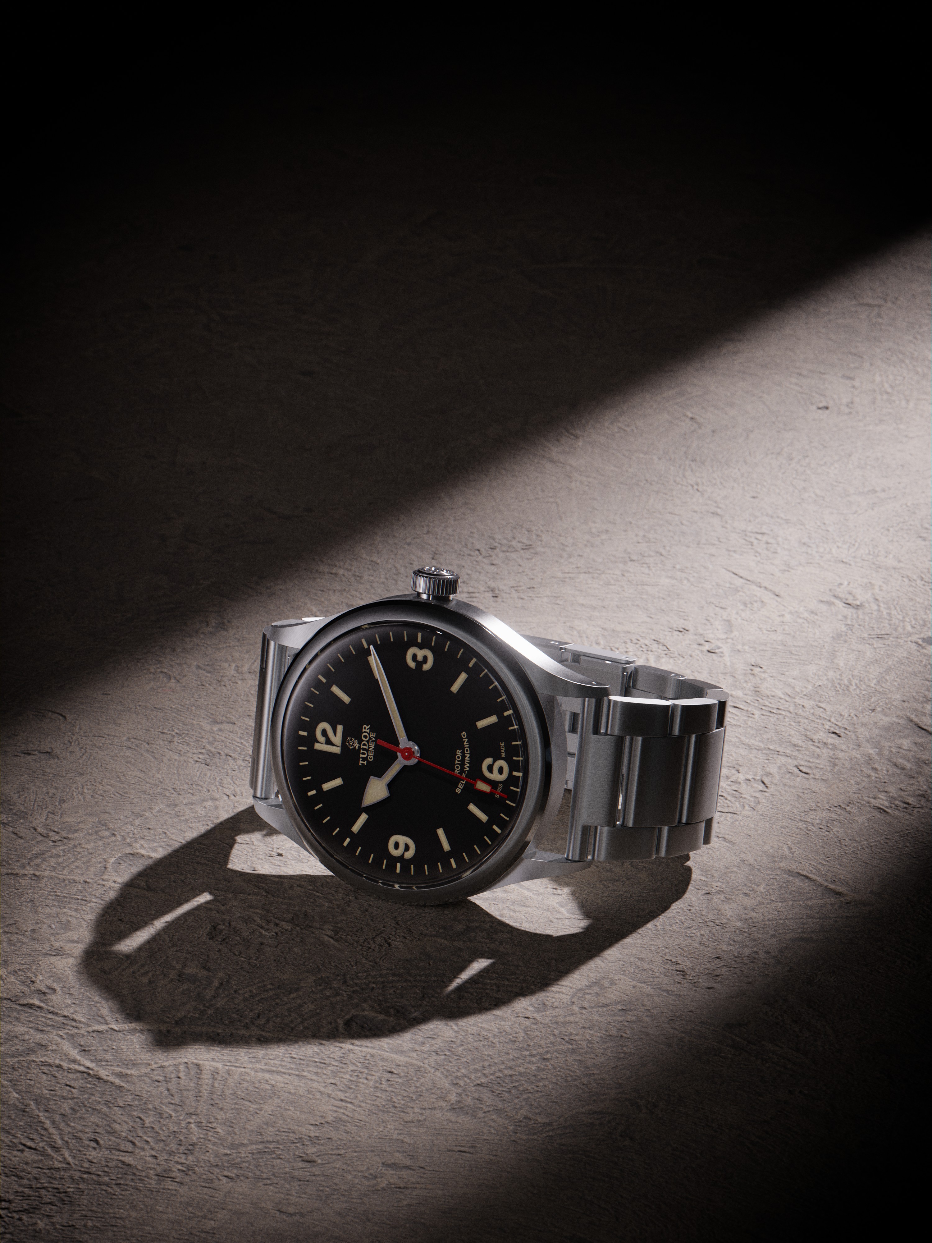 Tudor Heritage Ranger watch prominently displayed against a soft-focus background. The watch features a matte black dial with luminous hour markers and a brushed steel case, showcasing its elegant design. The image captures the watch in a well-lit setting, highlighting the craftsmanship and attention to detail, evoking a sense of luxury and sophistication.